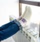 Una mujer se calienta los pies en el radiador frente a una ventana