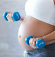 Close-up of pregnant woman doing exercise with dumbbells at home.