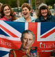 Royal fans pose with a Union Jack flag depicting Britain's King Charles III along the procession route, on The Mall, near to Buckingham Palace in central London, on May 5, 2023, ahead of the coronation weekend. - The country prepares for the coronation of Britain's King Charles III and his wife Britain's Camilla, Queen Consort on May 6, 2023. (Photo by Marco BERTORELLO / AFP)