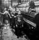 Old black and white archival photograph showing female worker and child labourers posing in spinning mill in the early twentieth century