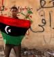 Un opositor a Gadafi sostiene una bandera nacional frente a una pintada en contra del líder libio