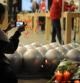 Una mujer toma fotografías con un iPhone a un improvisado arreglo de velas y flores al frente de una tienda de Apple en Santa Monica