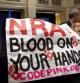 Una mujer despliega una pancarta en la que se puede leer "Asociación Nacional del Rifle. Sangre en vuestras manos", durante la rueda de prensa del presidente de la organización