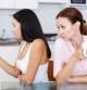 Young girl using her smartphone at kitchen table, her mother are near her