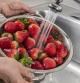 Una mujer lavando fresas bajo el grifo