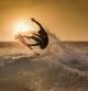 Surfer jumping on the wave at the golden hour on a tropical beach Sporty young man making tricks over the waves with a suf board Extreme sport and action in the water at the sunset with foam and spray (Surfer jumping on the wave at the golden hour on