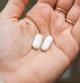 Close-up view of a hand holding two white pills in the palm above a blurry background