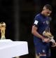 LUSAIL CITY, QATAR - DECEMBER 18: Kylian Mbappe of France walks past the FIFA World Cup Qatar 2022 Winner's Trophy as he is awarded the adidas Golden Boots award during the award ceremony following the FIFA World Cup Qatar 2022 Final match between Argentina and France at Lusail Stadium on December 18, 2022 in Lusail City, Qatar. (Photo by Clive Brunskill/Getty Images)