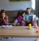 LECTURA EN FAMILIA. UN PADRE LEE UN LIBRO A SUS DOS HIJAS EN EL COMEDOR DE SU CASA