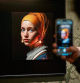 A visitor takes a picture with his mobile phone of an image designed with artificial intelligence by Berlin-based digital creator Julian van Dieken (C) inspired by Johannes Vermeer's painting 