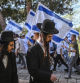 Two ultra Orthodox men walk past religious Israeli pre-military aged youth, wave their national flag as they protest outside the Old City of Jerusalem in support of Israel on October 26, 2023, amid the ongoing battles between Israel and the Palestinian group Hamas. Thousands of civilians, both Palestinians and Israelis, have died since October 7, 2023, after Palestinian Hamas militants based in the Gaza Strip entered southern Israel in an unprecedented attack triggering a war declared by Israel on Hamas with retaliatory bombings on Gaza. (Photo by Aris MESSINIS / AFP)