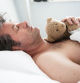 Man sleeping with his bear on his chest, hand on paw.