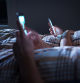 Bored distant couple ignoring each other lying in bed at night while using mobile phones. Smartphone addict. Obsessed and distracted man and woman texting. Addiction to social media and technology.