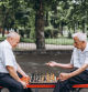 Two senior adult men playing chess on the bench outdoors in the park