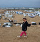 A displaced Palestinian girl poses for a picture as she walks next to a makeshift camp housing displaced Palestinians in Khan Yunis, in the southern Gaza Strip on December 31, 2024, amid the continuing war between Israel and the militant Hamas group. The majority of Gaza's 2.4 million people have been displaced, often multiple times, by the war that began with Hamas's attack on southern Israel on October 7, 2023. With many displaced living in tent camps, the coming winter is raising serious concerns. (Photo by BASHAR TALEB / AFP)