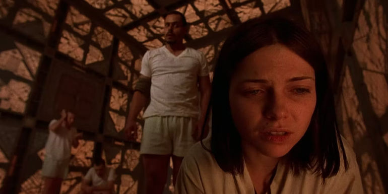 Leaven looks down at the ground and Quintin stands over her in the movie Cube.