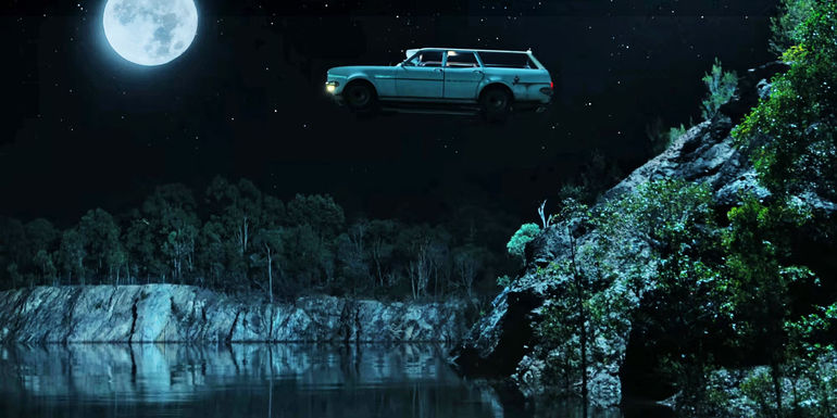 Car floating in air over a cliffside lake with bright full moon in the dark sky