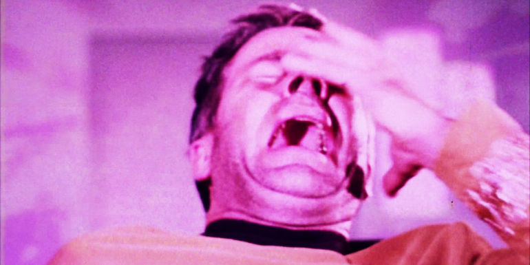 Decker throws a hand up to his face as he's engulfed by purple light