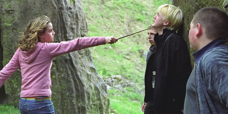 Hermione (Emma Watson) pointing a wand at Draco's (Tom Felton) neck as Crabbe and Goyle watch in Harry Potter and the Prisoner of Azkaban.