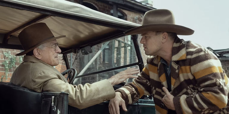 William is in his car, reaching for Ernest who is standing outside his car in Killers of the Flower Moon.