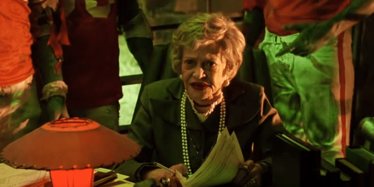 Juno (Sylvia Sidney) going through paperwork with the football players behind her in her office in Beetlejuice