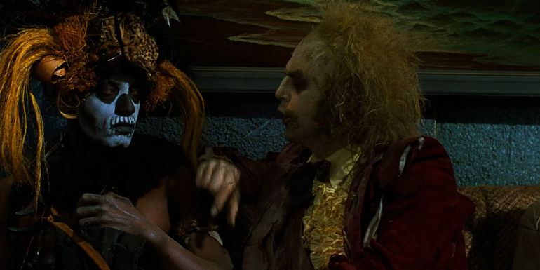 Beetlejuice taps a witch doctor on the shoulder while talking in Beetlejuice.