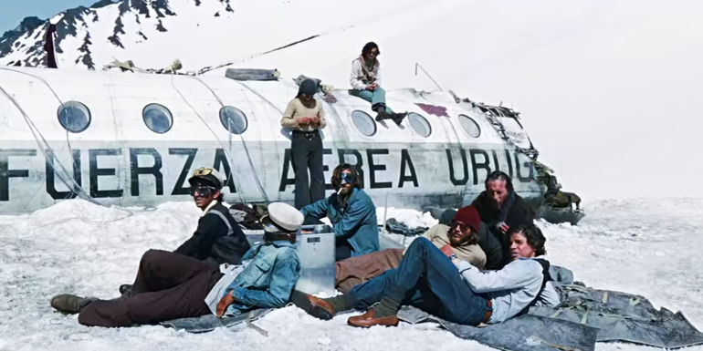 Several survivors sitting outside of the ruined plane in Society of the Snow