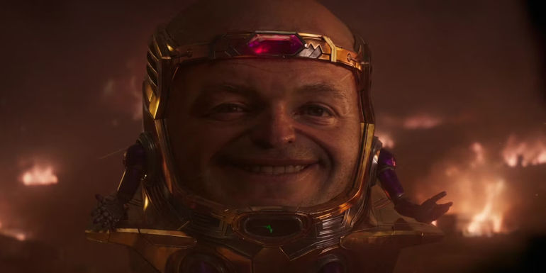 Corey Stoll as MODOK smiling in front of flames in Ant-Man and the Wasp: Quantumania (2023)