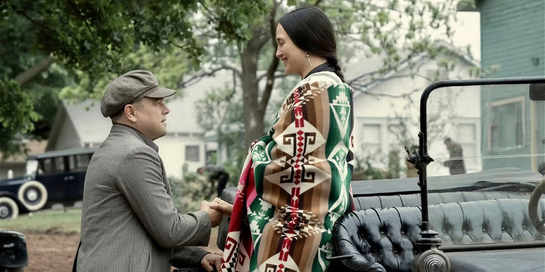 Ernest (Leonardo DiCaprio) is on one knee in front of Mollie (Lily Gladstone) next to a car in Killers of the Flower Moon. 