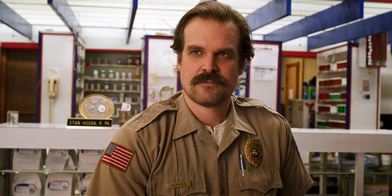 David Harbour as Jim Hopper looking to the side and smiling in Stranger Things. 