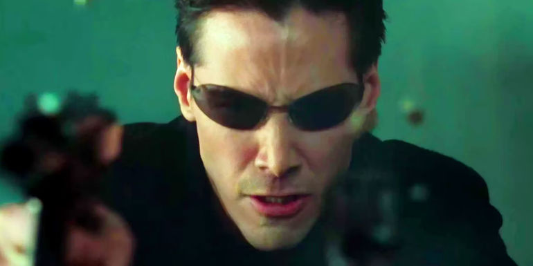 Keanu Reeves as Neo Wearing Sunglasses and Holding Two Guns in The Matrix
