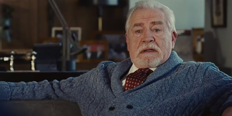 Logan Roy spreading his arms in Succession, sitting down in his office, wearing a sweater and speaking angrily.