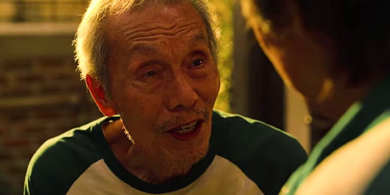 Oh Il-nam talks to Gi-hun during the marbles task in Squid Game.