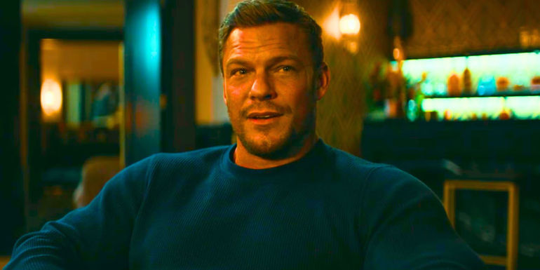 Alan Ritchson as Reacher sitting in a fancy hotel room