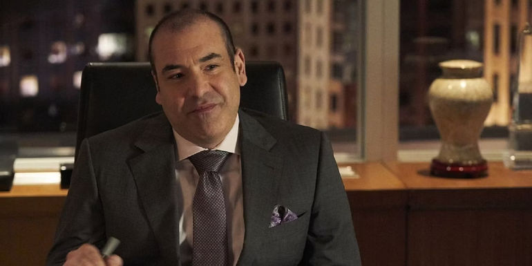 Louis smiling behind his desk in Suits