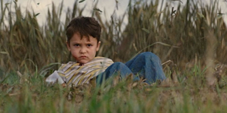 Pierce Gagnon lying injured in a field and looking angry as Cid in Looper
