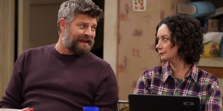 Jay R Ferguson's Ben Olinsky sits beside Sara Gilbert's Darlene and smiles in the kitchen on The Conners