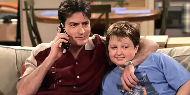 Charlie (Charlie Sheen) talking on the phone with his arm around Jake (Angus T. Jones) on Two and a Half Men