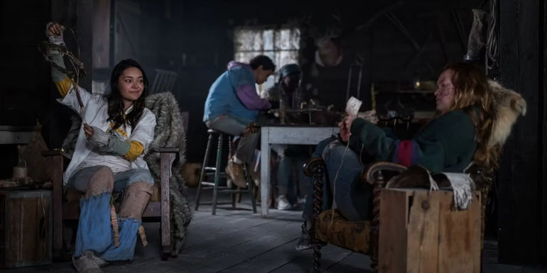 One girl smiling and showing another girl a crafted item in the cabin in Yellowjackets season 2 episode 3.