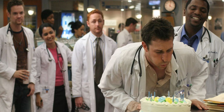 Carter blowing out candles on a cake with Neela and Morris behind him in ER season 11