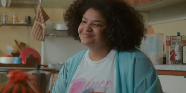 Tilly smiles whiles standing in the kitchen in One Day.