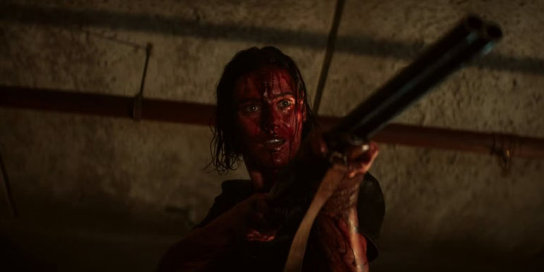 Lilly Sullivan covered in blood pointing a gun in Evil Dead Rise