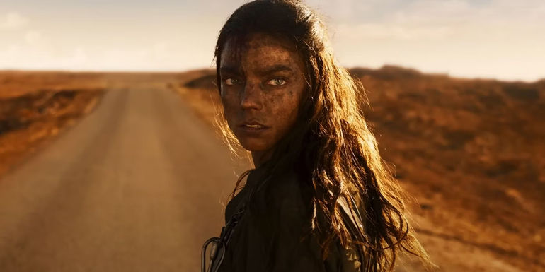 Furiosa (Anya Taylor-Joy) looks over her left shoulder at an unknown person while standing in the middle of the open road in Furiosa