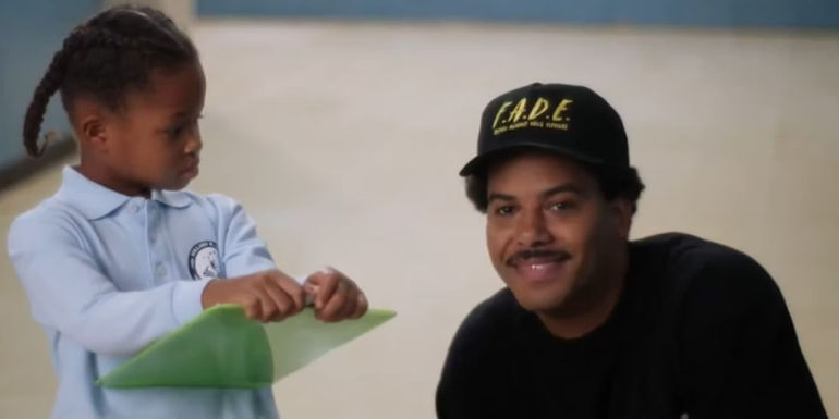 Tariq (Zack Fox) smiling at the camera while a chold holds a clipboard and stares at him in Abbott Elementary.