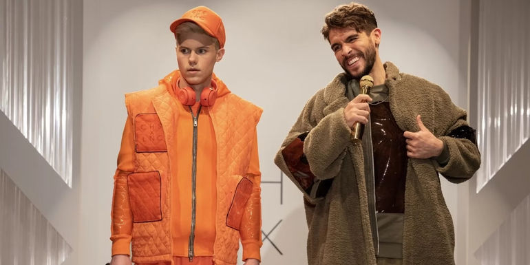 Lance (Josh Segarra) smiles while holding a mic and standing next to a concerned-looking Chase (Case Walker) in The Other Two.