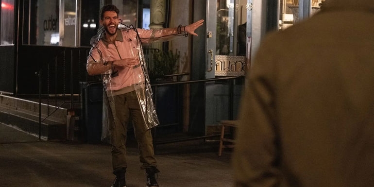 Lance (Josh Segarra) smiles while dabbing in a clear raincoat outside a restaurant in The Other Two.