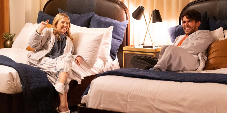 Brooke (Helene Yorke) and Lance (Josh Segarra) laugh while sitting on side-by-side beds in The Other Two.