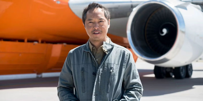 Topher (Ken Leung) standing in front of a plane and smiling in The Night Shift.