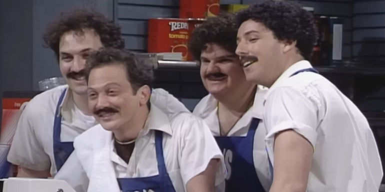 Rob Schneider, Adam Sandler, Chris Farley, and Robert Smigel in chef outfits and black wigs smiling in Hub's Gyro in SNL.