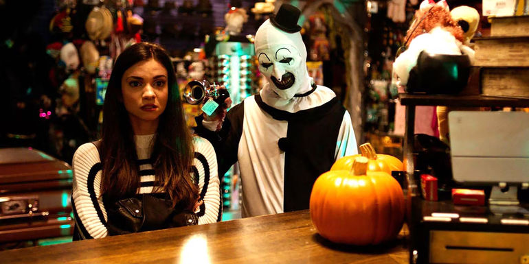 Art the Clown stands behind Lauren LeVara at a bar in Terrifier 2 - The Next Terrifier Movie Arrives In October 2024 - Terrifier 3 Release Date